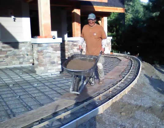 Ed Garmon pushing a wheelbarrow of concrete across rebar on a curved patio form